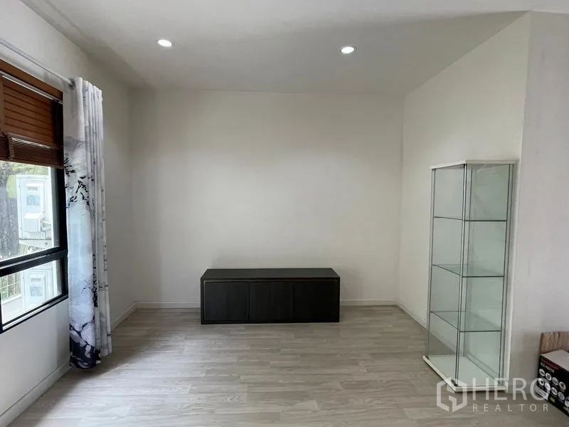 Townhouse for rent in Bang Kapi, Bangkok - Minimal room with glass display cabinet and low TV console by the window.