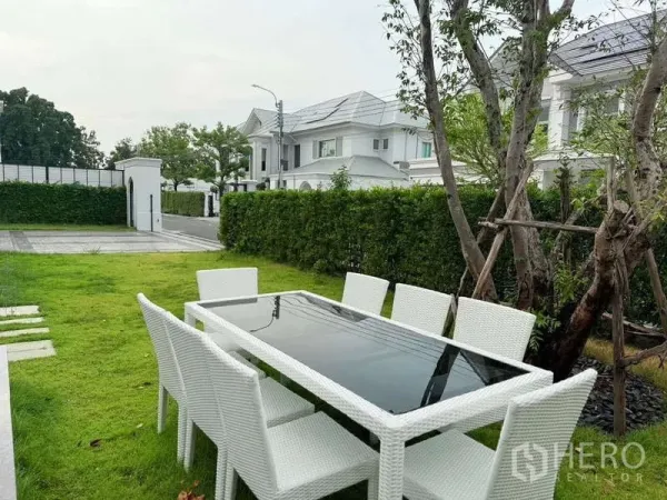 Detached House for rent or sale in Bang Phli, Samut Prakan - Lawn garden with white outdoor dining table and chairs facing a quiet gated community street.