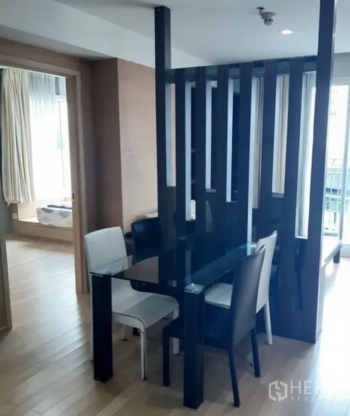 Condominium for rent in Khlong Toei, Bangkok - Dining nook with glass table and mixed chairs beside a decorative partition.