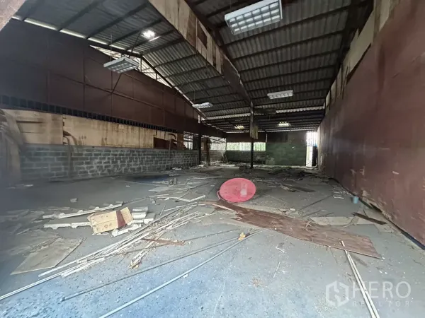 Warehouse for rent or sale in Yan Nawa, Bangkok - Deep interior bay with high ceiling, fluorescent lights and a gated rear wall, debris on the floor.