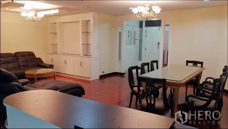 Condominium for rent or sale in Khlong Toei, Bangkok - Spacious living and dining area with leather sectional sofa, six-seat dining table, and built-in shelving.