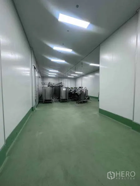 Factory for rent - GMP-grade cleanroom corridor with green epoxy flooring and stainless tanks under bright LED lighting.