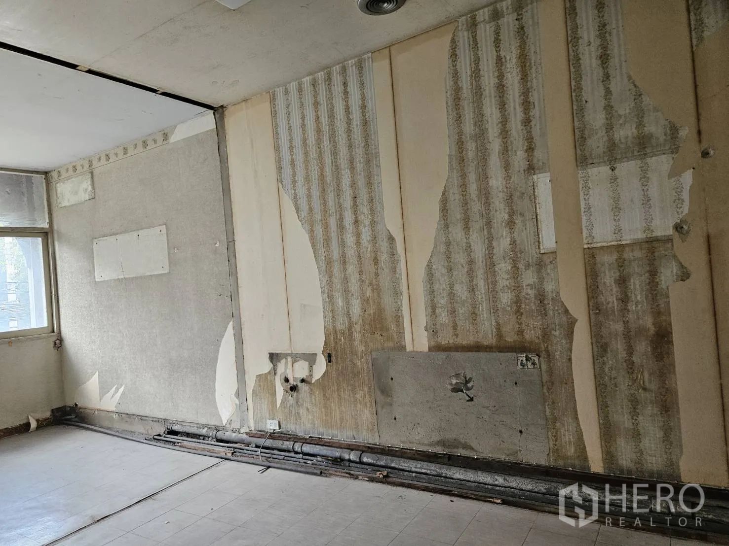 Shophouse for rent in Watthana, Bangkok - Detail of interior wall showing peeling wallpaper and exposed conduits for services.