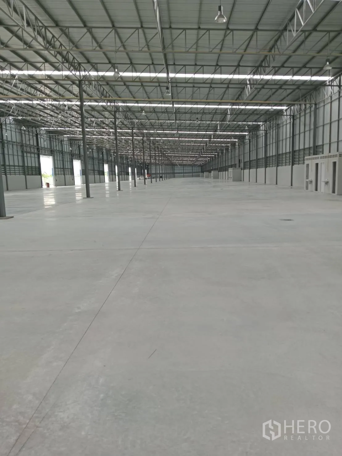 Warehouse for rent in Lat Krabang, Bangkok - Long warehouse hall with concrete flooring, rows of support columns, and hanging industrial lights.