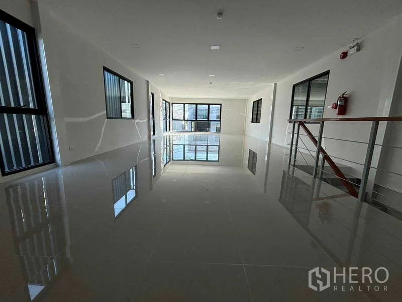 Factory for rent in Bang Bo, Samut Prakan - Open‑plan upper office with shiny tiled flooring, multiple black‑framed windows and fire safety fixtures.