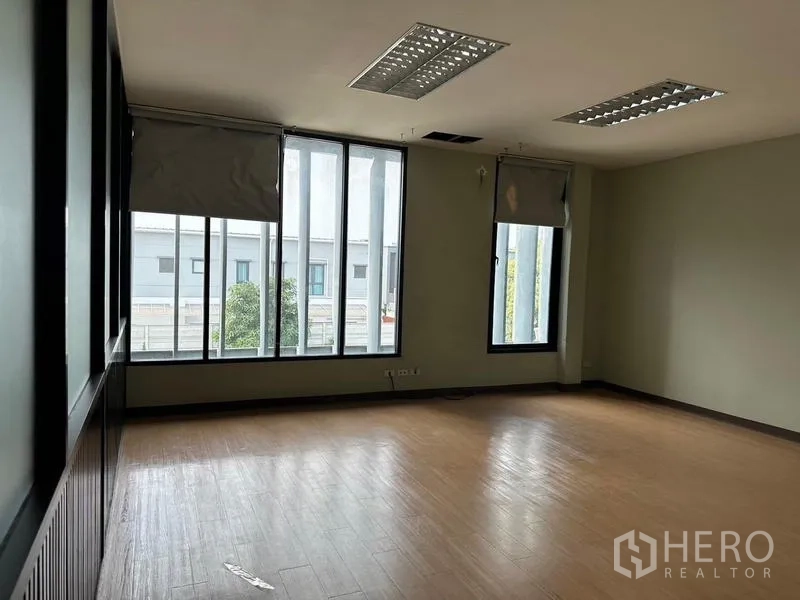 Warehouse for rent in Prawet, Bangkok - Empty office room with large vertical windows and wood-look flooring.