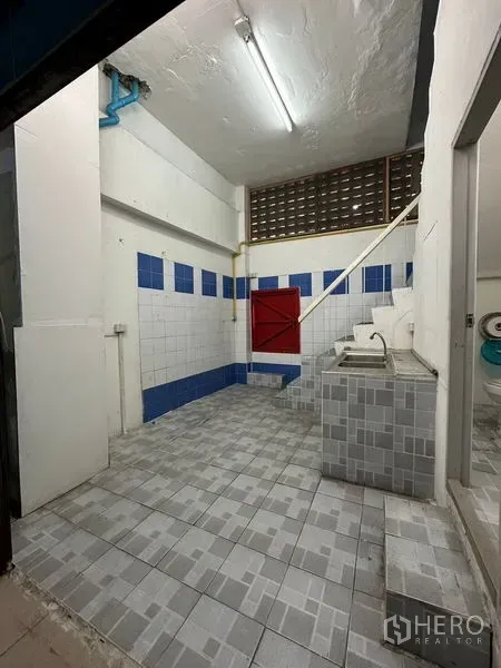 Shophouse for rent in Bang Na, Bangkok - Rear utility area with tiled walls, sink and staircase access inside the shophouse.