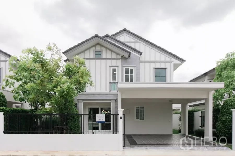Detached House for rent or sale in Bang Phli, Samut Prakan - Front view of a modern white two-storey detached house with a gated fence and covered carport.