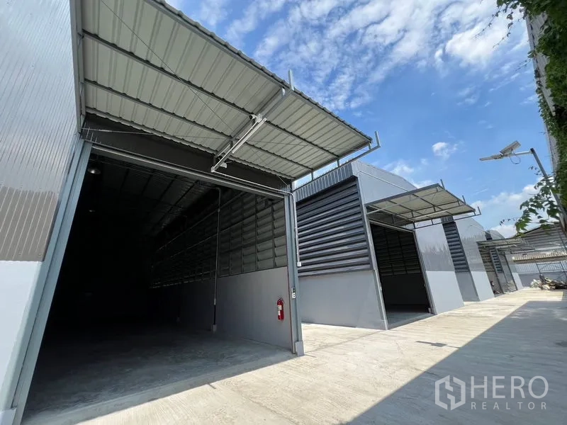 Warehouse for rent in Prawet, Bangkok - Modern grey warehouse bays with large roll‑up doors and covered loading canopies along a wide concrete drive.