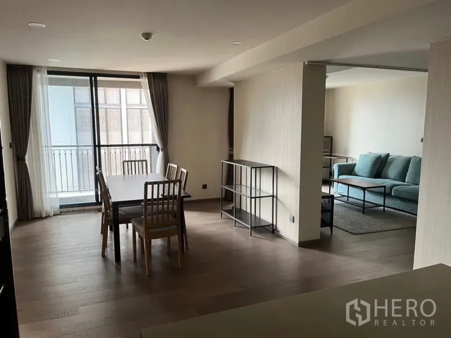 Condominium for rent in Pathum Wan, Bangkok - Dining area opening to a balcony and adjacent lounge with a teal sofa in a minimalist condo interior.