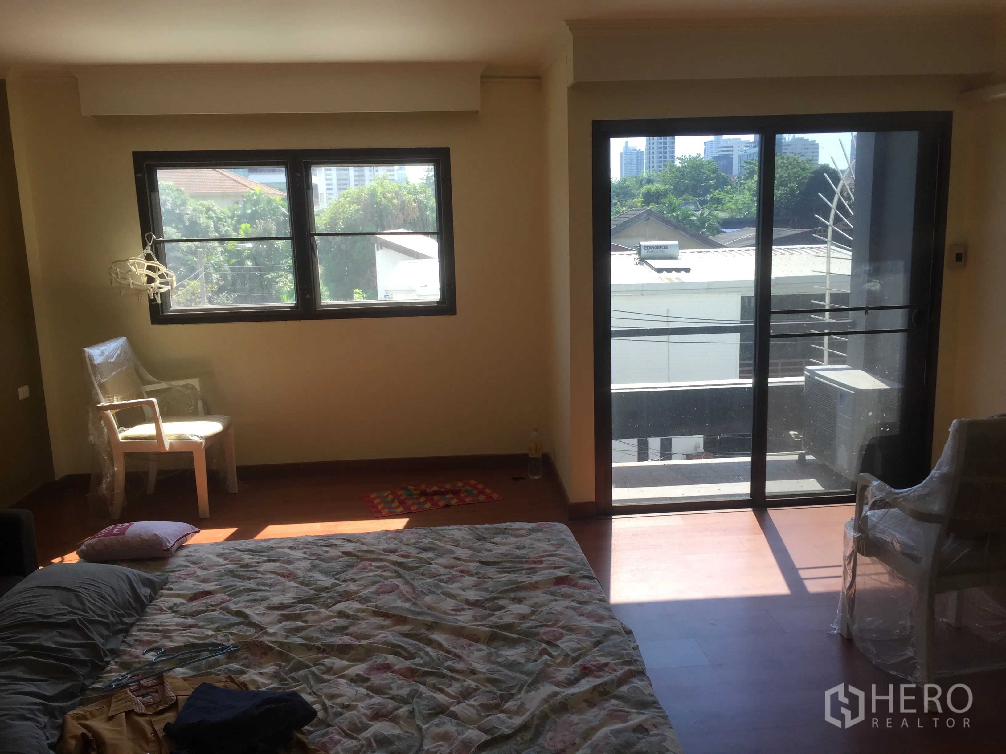 Townhouse for rent in Khlong Toei, Bangkok - Sunlit bedroom with wood floors, a window and sliding glass door opening to a small balcony.