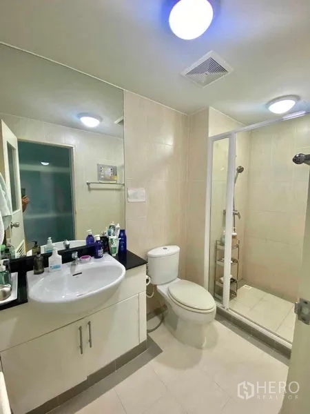 Condominium for rent in Watthana, Bangkok - Modern bathroom with vanity, toilet, and a glass-enclosed walk-in shower under ceiling lights.