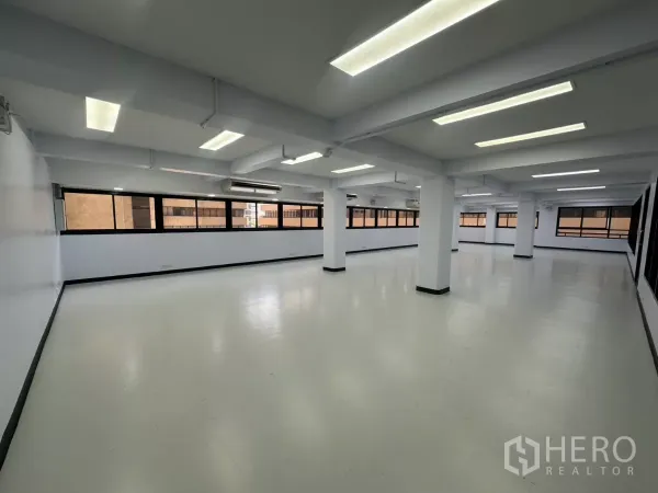 Office Space for rent - Open-plan office with white floors, support columns, long strip windows and bright LED ceiling lights.