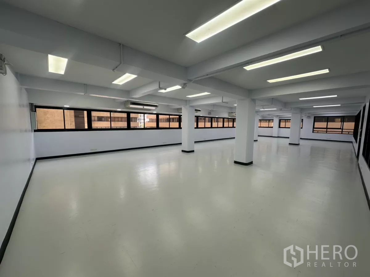 Office Space for rent - Open-plan office with white floors, support columns, long strip windows and bright LED ceiling lights.