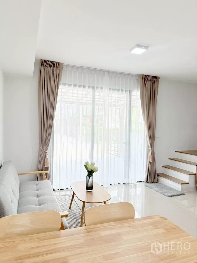 Townhouse for rent in Bang Phli, Samut Prakan - Living area with large sliding glass doors, sheer curtains and staircase.