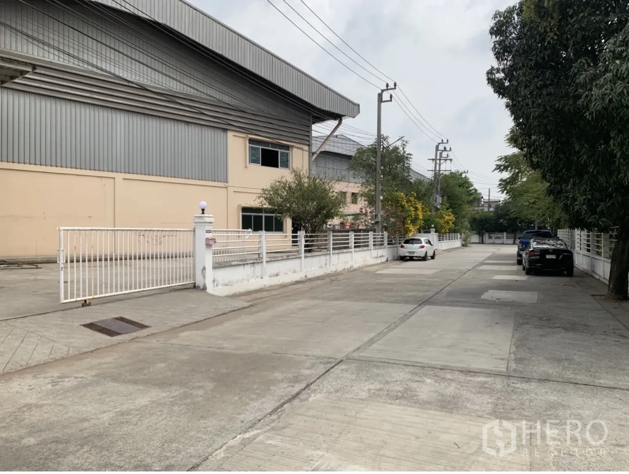 Factory for rent in Mueang Samut Prakan, Samut Prakan - Quiet access road beside the factory with parking spaces and a secure perimeter fence.