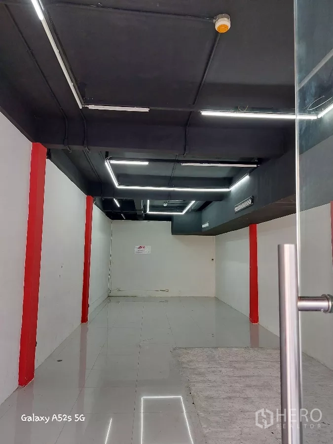 Retail Space for rent in Khlong Toei, Bangkok - Long open-plan shop interior with glossy tiled floor, white walls, red columns and black ceiling with LED strip lights.