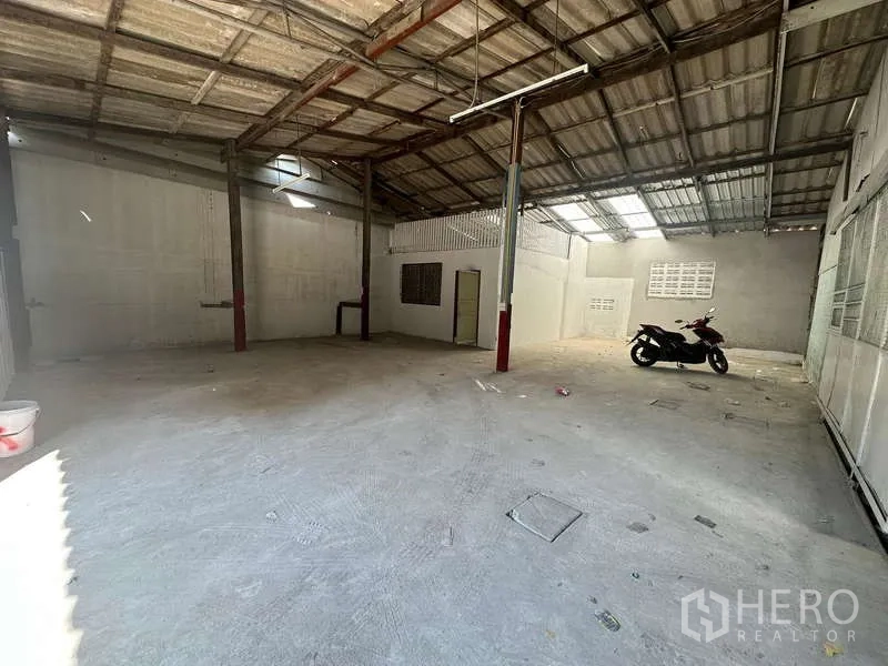 Warehouse for rent in Suan Luang, Bangkok - Bright loading zone with steel roof, skylight panels and a scooter parked by the wall.