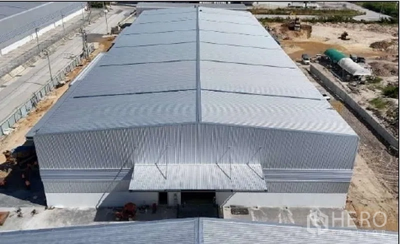 Warehouse for rent in Mueang Rayong, Rayong - Aerial view of a large modern warehouse with metal roof, loading canopies and paved yard in an industrial area.