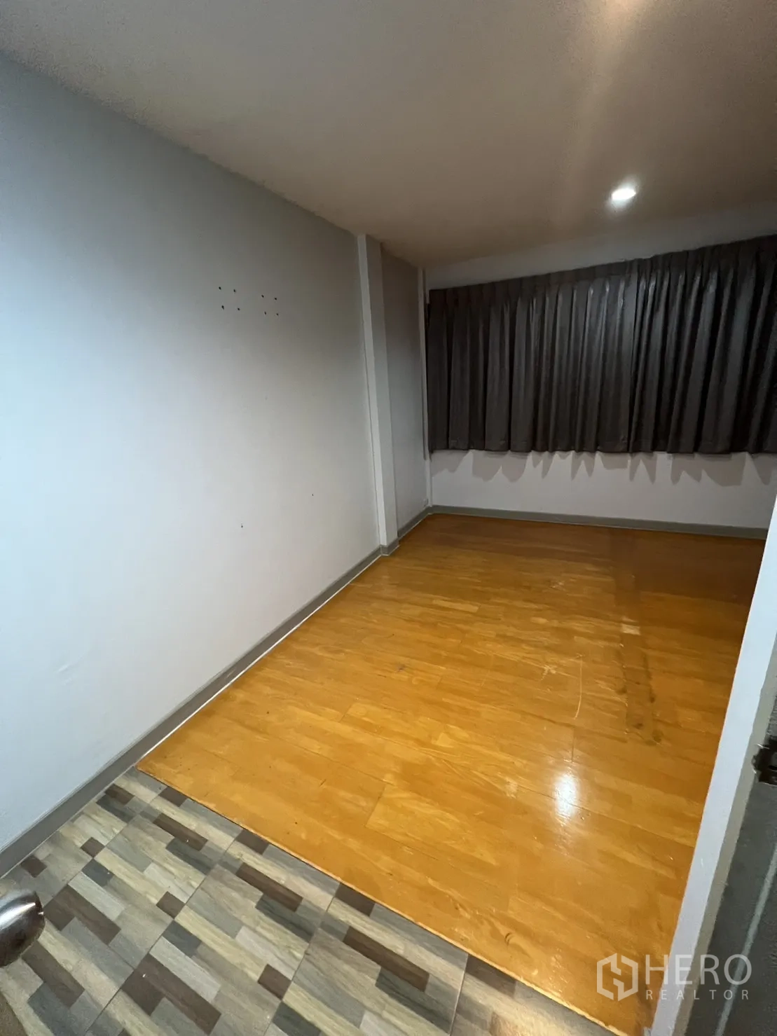 Townhouse for rent in Watthana, Bangkok - Compact room with wood laminate floor and dark curtains.