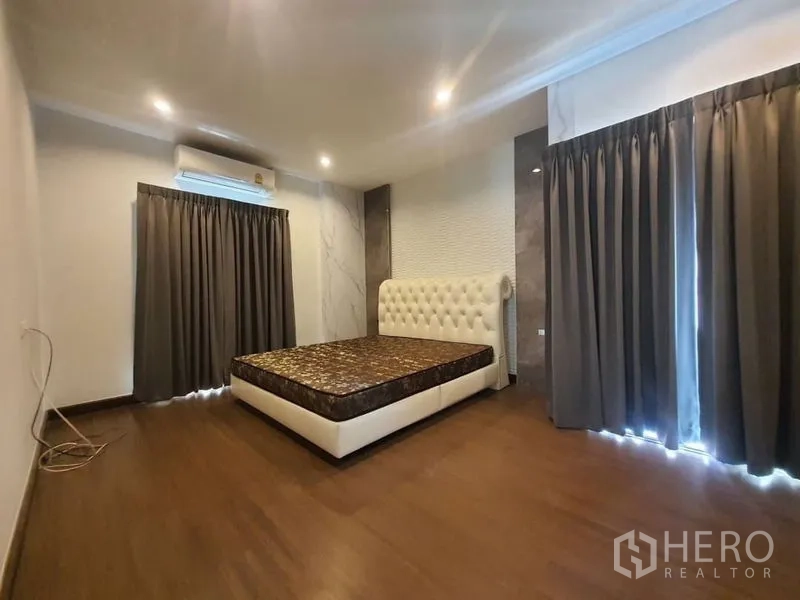 Detached House for rent in Prawet, Bangkok - Spacious bedroom with AC, floor-to-ceiling curtains and white tufted headboard bed.