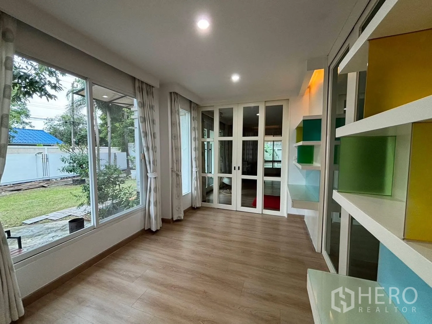 Detached House for rent in Bang Kapi, Bangkok - Sunroom with floor-to-ceiling windows and garden view, colorful shelves.
