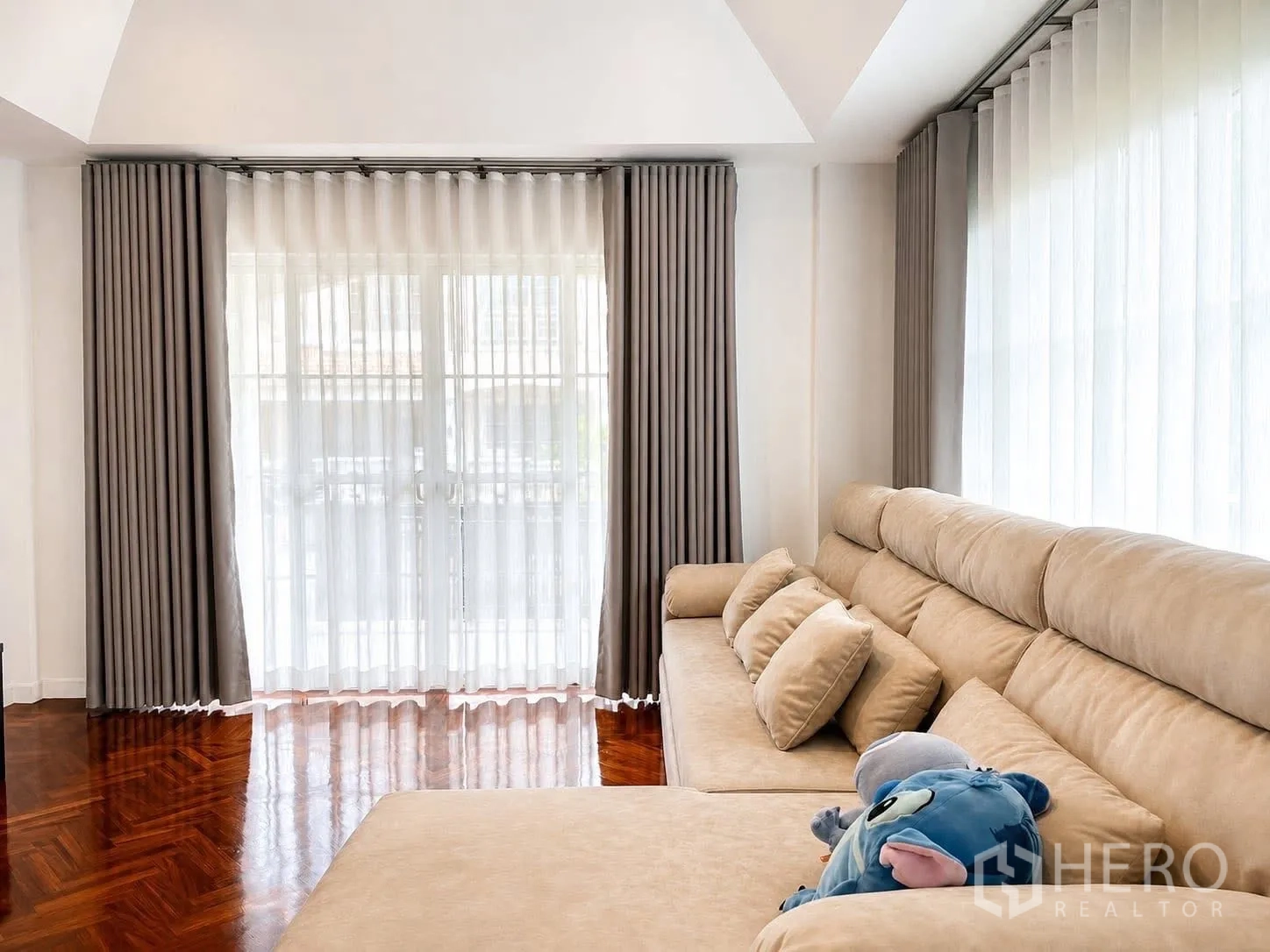 Detached House for rent in Prawet, Bangkok - Living room featuring a large beige sectional sofa and two sets of glass doors with curtains.