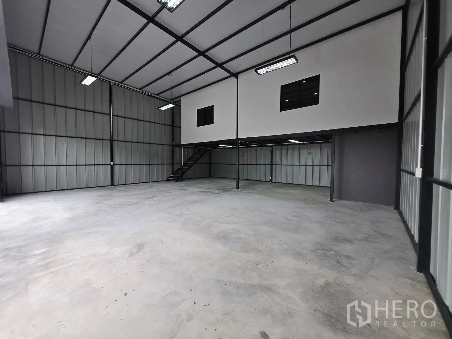 Warehouse for rent - Open industrial hall showing a two-storey office box and staircase with hanging LED lights.
