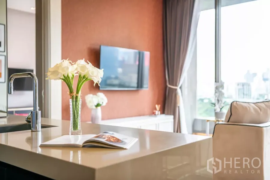 Condominium for rent or sale in Bang Rak, Bangkok - Bright Bang Rak condo kitchen island with chrome faucet, flowers, and living area facing park and skyline views.