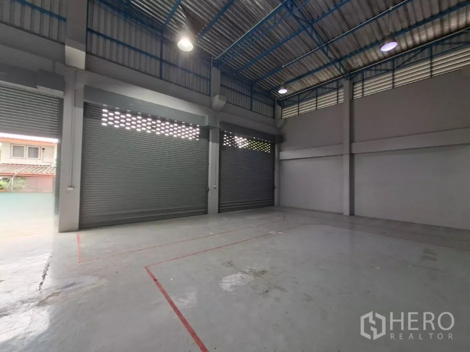 Warehouse for rent in Suan Luang, Bangkok - Spacious storage area featuring multiple shutter doors and painted loading zone markings.
