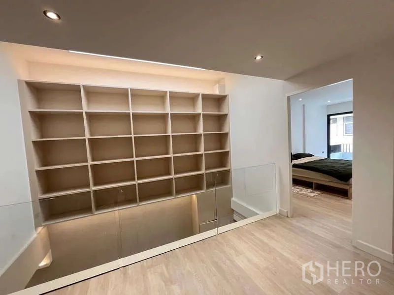 Townhouse for sale in Khlong Toei, Bangkok - Mezzanine with glass balustrade and illuminated shelving leading to a bedroom.