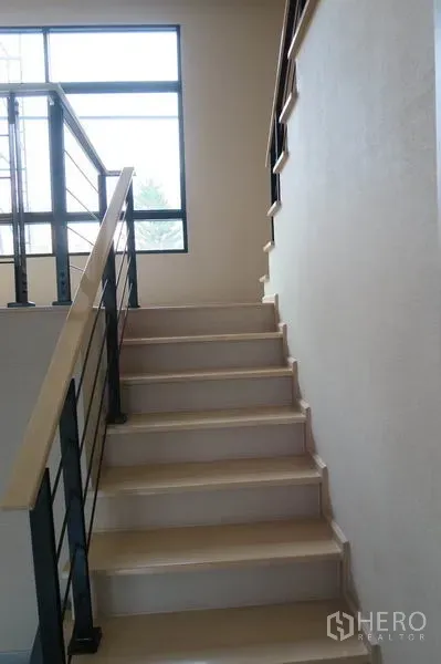Townhouse for rent in Suan Luang, Bangkok - Close-up of light-wood staircase with black metal handrails leading upstairs.