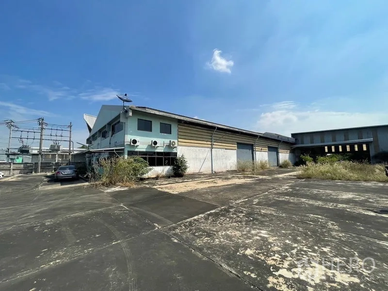 Warehouse for rent or sale in Bang Bon, Bangkok - Side exterior of the warehouse with loading shutters and an expansive paved yard.