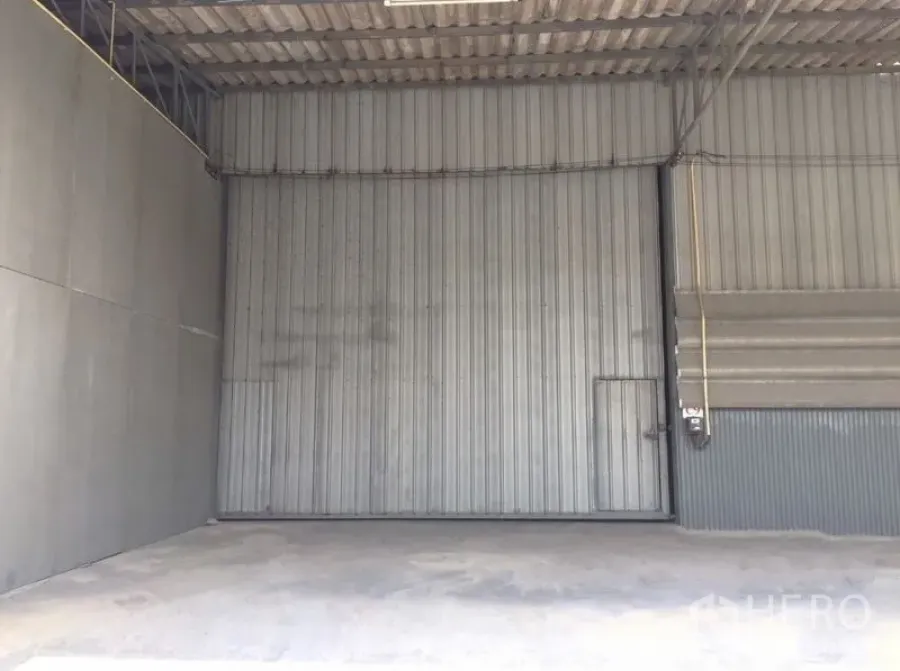 Warehouse for rent in Prawet, Bangkok - Interior of warehouse with large corrugated metal sliding door and smooth concrete floor.