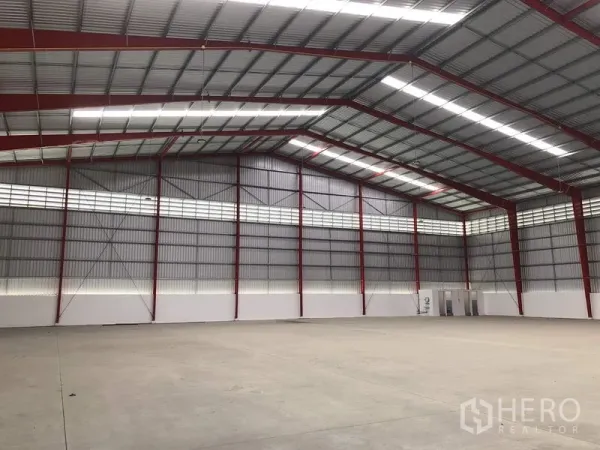 Warehouse for rent in Pak Kret, Nonthaburi - Spacious warehouse interior with red steel frames, skylight strips and concrete floor.