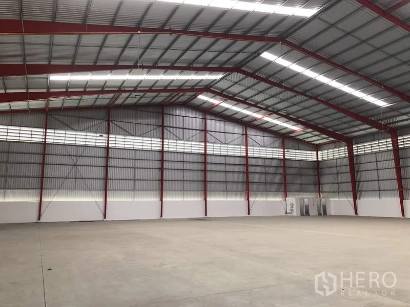 Warehouse for rent in Pak Kret, Nonthaburi - Spacious warehouse interior with red steel frames, skylight strips and concrete floor.