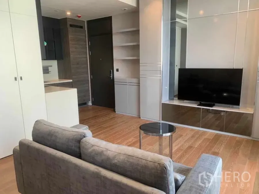 Condominium for rent in Pathum Wan, Bangkok - Open‑plan living area with sofa, wall‑mounted TV unit and storage facing the kitchen in a Bangkok condo.