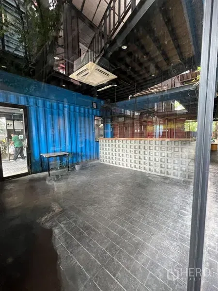 Retail Space for rent - Open-plan shop space with high ceiling, blue container walls and a lit bar viewed through glass.