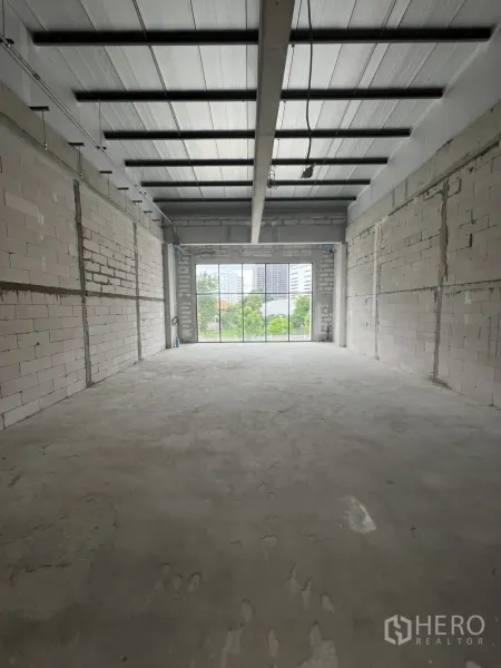 Retail Space for rent in Khlong Toei, Bangkok - Shell retail interior with bare concrete floor, brick walls and high metal ceiling facing a large window.