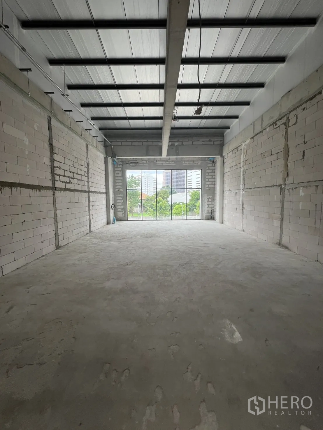Retail Space for rent in Khlong Toei, Bangkok - Shell retail interior with bare concrete floor, brick walls and high metal ceiling facing a large window.