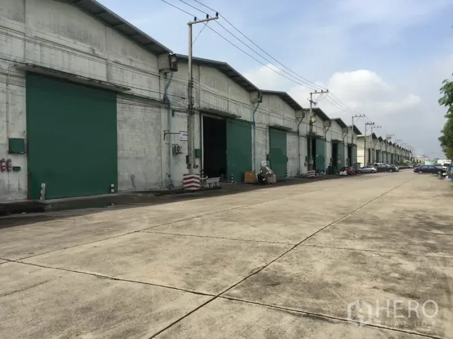 Warehouse for rent in Khlong Luang, Pathum Thani - Row of warehouses with green shutters along a wide driveway suitable for trucks.