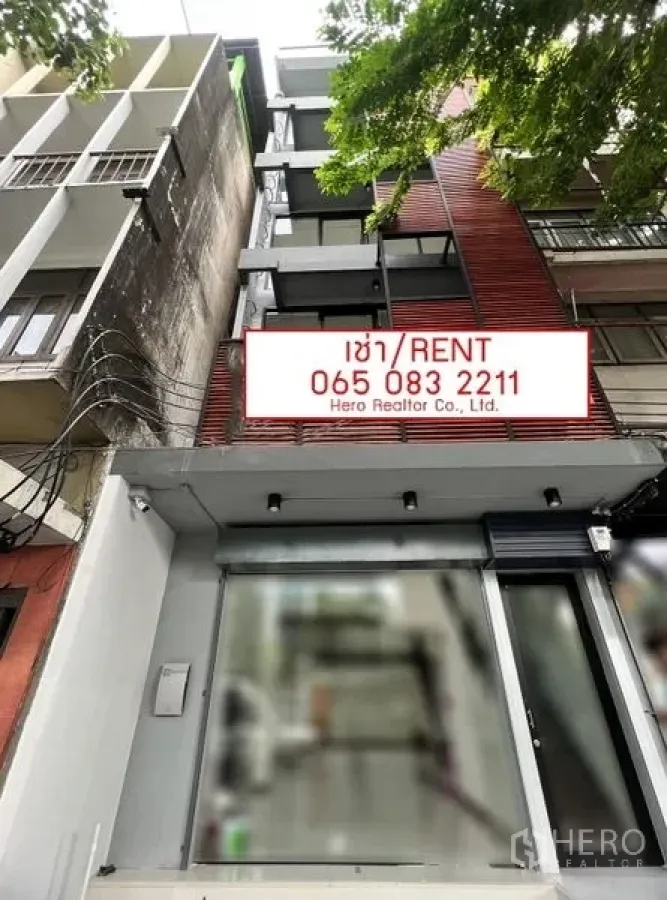 Shophouse for rent in Khlong Toei, Bangkok - Shophouse exterior with glass frontage and a visible for-rent sign on a tree-lined street.