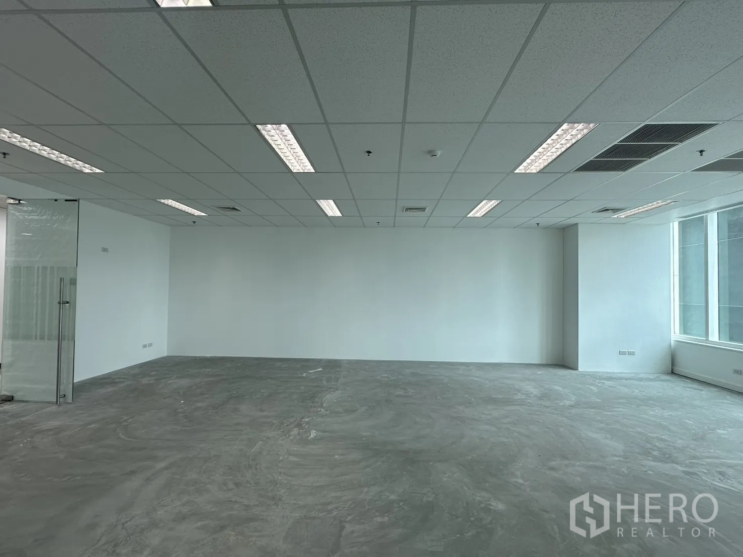Office Space for rent in Watthana, Bangkok - Spacious unfurnished office showing glass entry door, drop ceiling lighting, and concrete floor.
