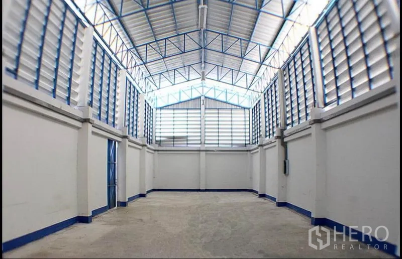 Factory for rent in Pak Kret, Nonthaburi - High-ceiling warehouse hall with steel trusses, louvered ventilation and concrete floor.