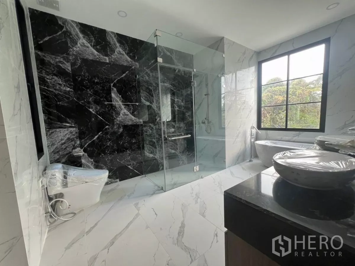 Detached House for rent in Lat Phrao, Bangkok - Luxurious bathroom with glass shower enclosure, freestanding bathtub, double vanity and marble-effect tiles.