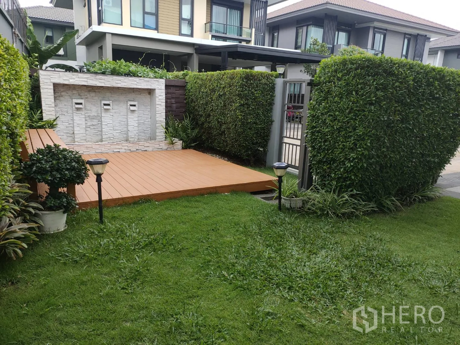 Detached House for rent or sale in Lam Luk Ka, Pathum Thani - Landscaped corner garden with wooden deck and stone feature wall with water spouts.