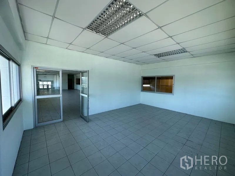 Factory for rent in Chon Buri - Tiled office room with suspended ceiling, fluorescent lighting, and sliding glass doors.