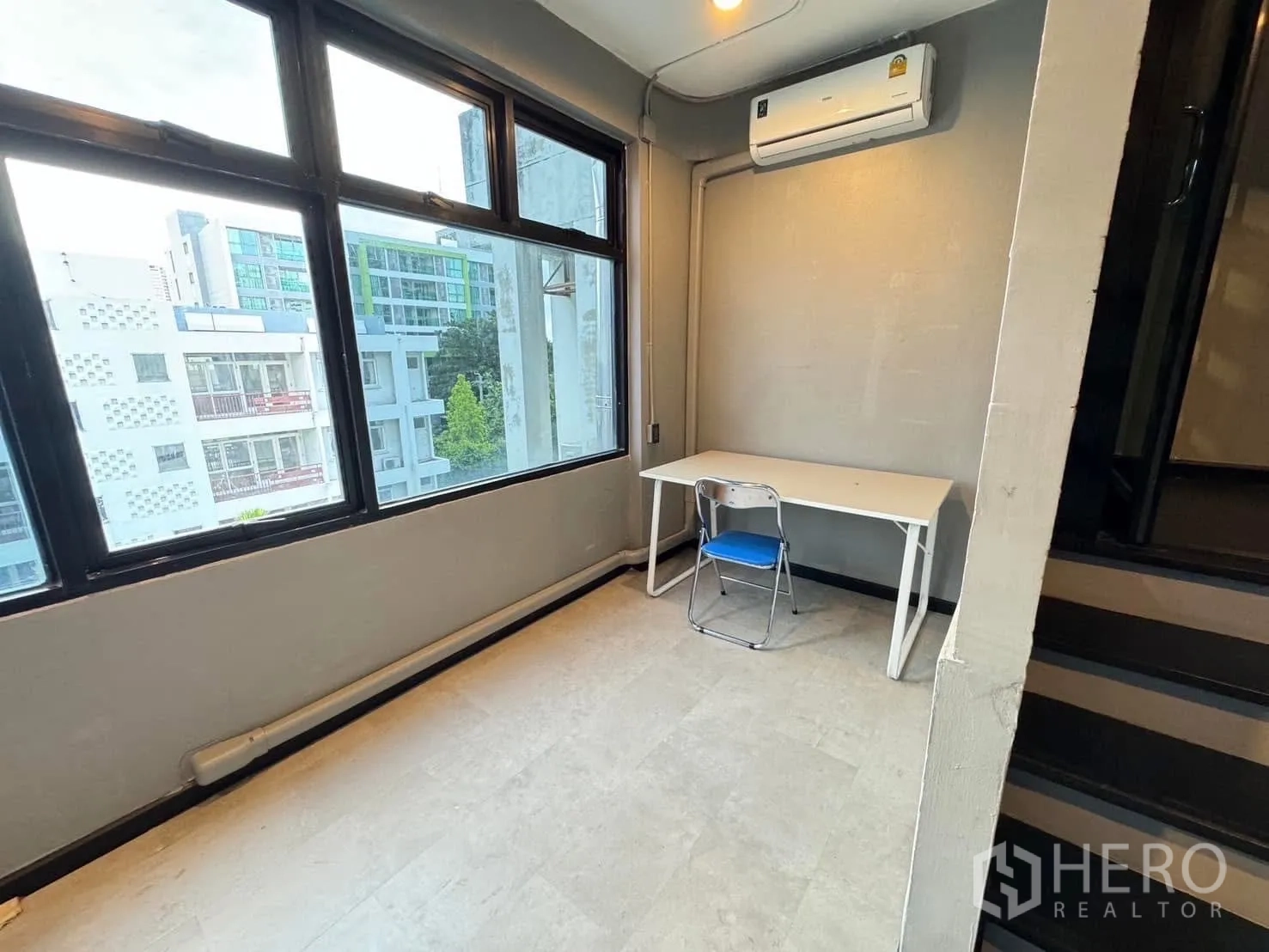 Home Office for rent in Watthana, Bangkok - Corner workspace with large windows, a small desk and wall-mounted air-conditioner.