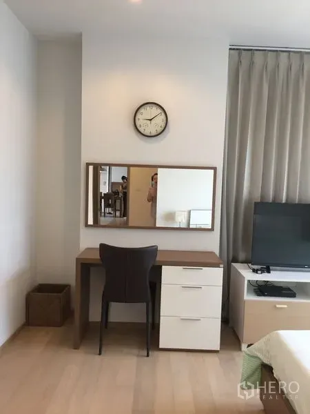 Condominium for rent in Watthana, Bangkok - Work and vanity corner with desk, drawers, wall mirror and clock beside a window.