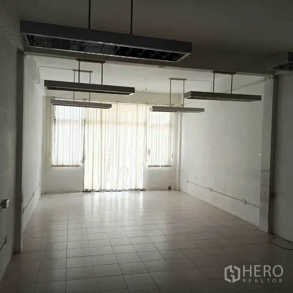 Shophouse for rent in Khlong Toei, Bangkok - Open-plan floor with hanging fluorescent lights and floor-to-ceiling blinds.